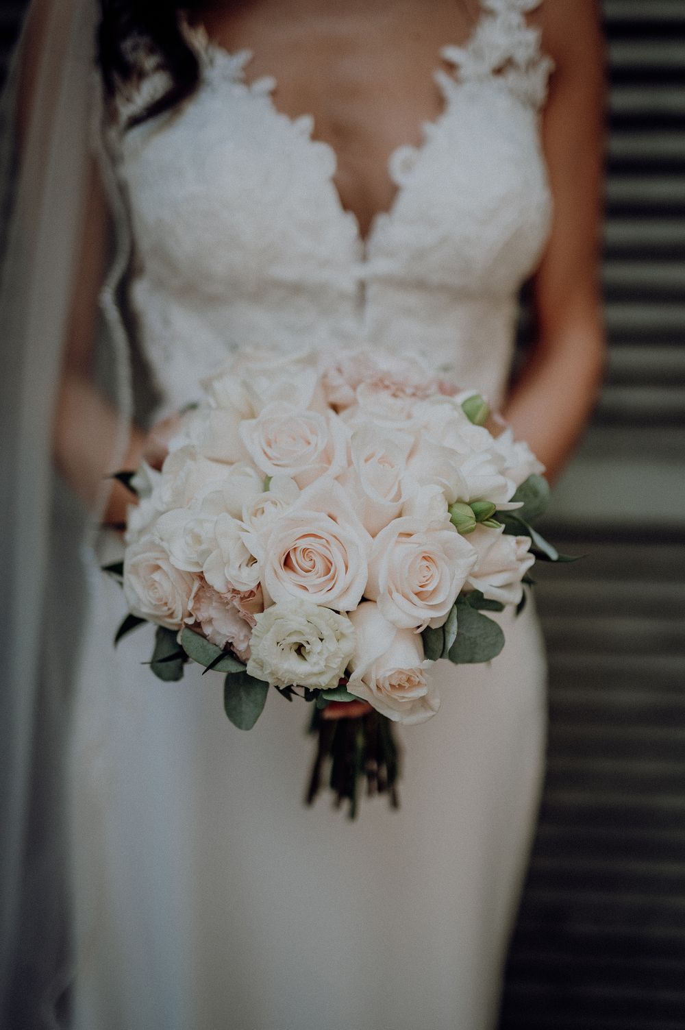 Close-up of a bridal bouquet of blush and white roses held by a bride in lace.