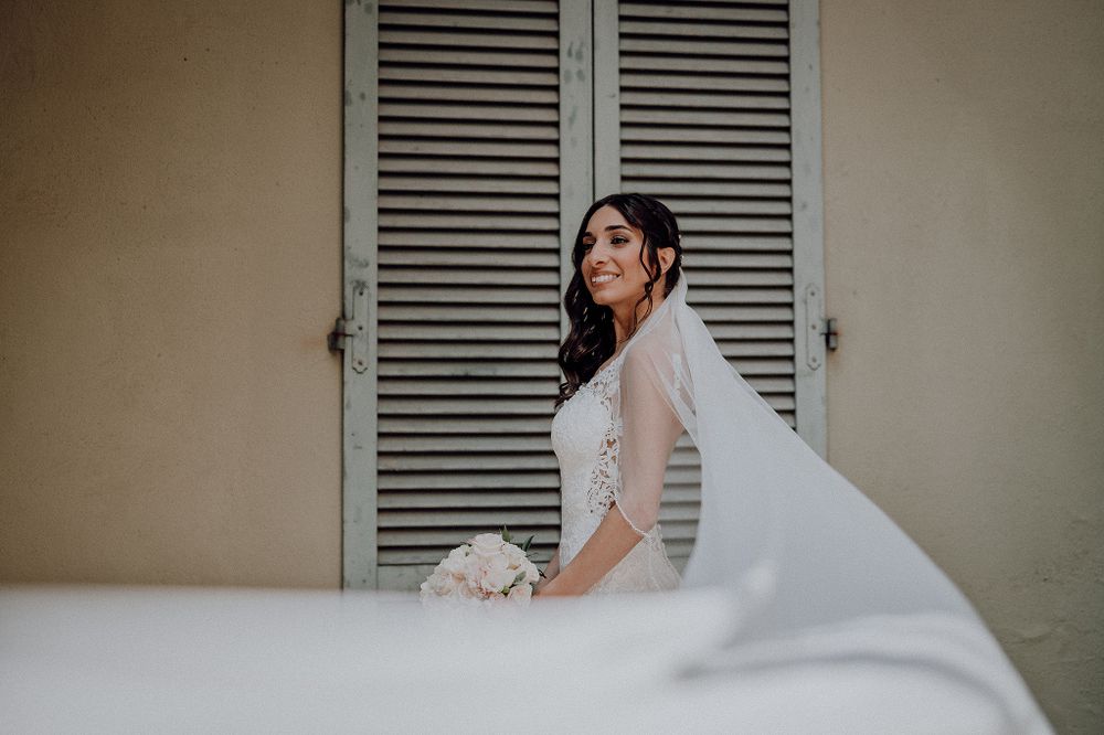 Radiant bride in a lace wedding gown with veil posing near vintage shuttered doors.