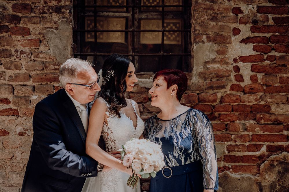 Bride sharing a tender moment with her parents against a rustic brick wall backdrop.
