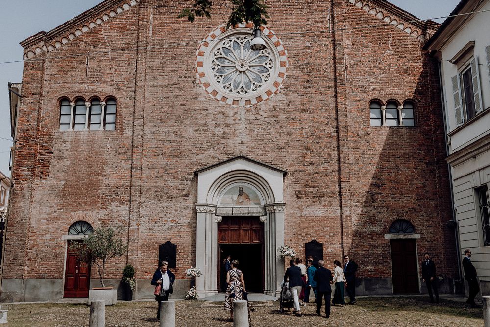 Wedding guests gather outside a historic red brick church with a stunning rose window for a ceremony.