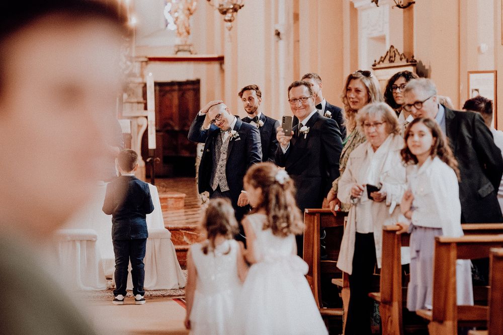 Joyful wedding guests smile and photograph the bride walking down the aisle of a beautiful ornate church.