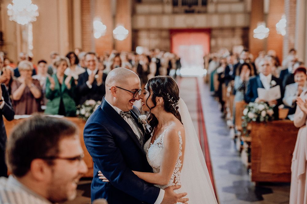 Bride and groom sharing first kiss at church altar while guests applaud in background.