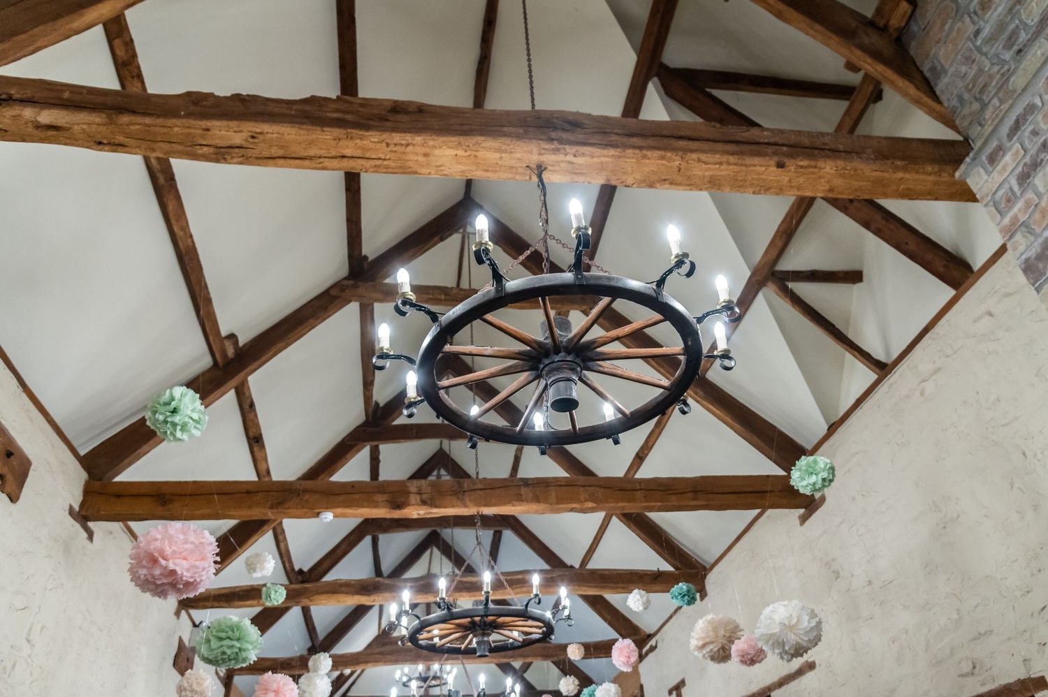 Exposed wooden beam ceiling with rustic wagon wheel chandelier in a converted barn venue.