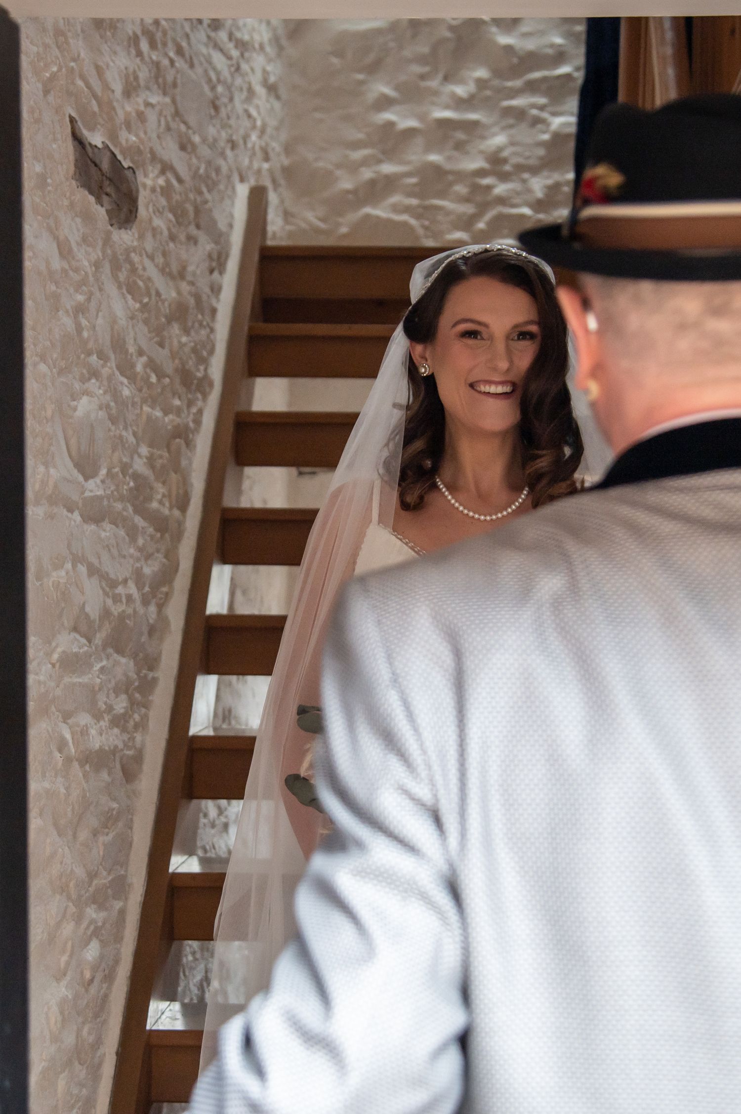 First look moment captured in rustic stone-walled venue with wooden staircase.