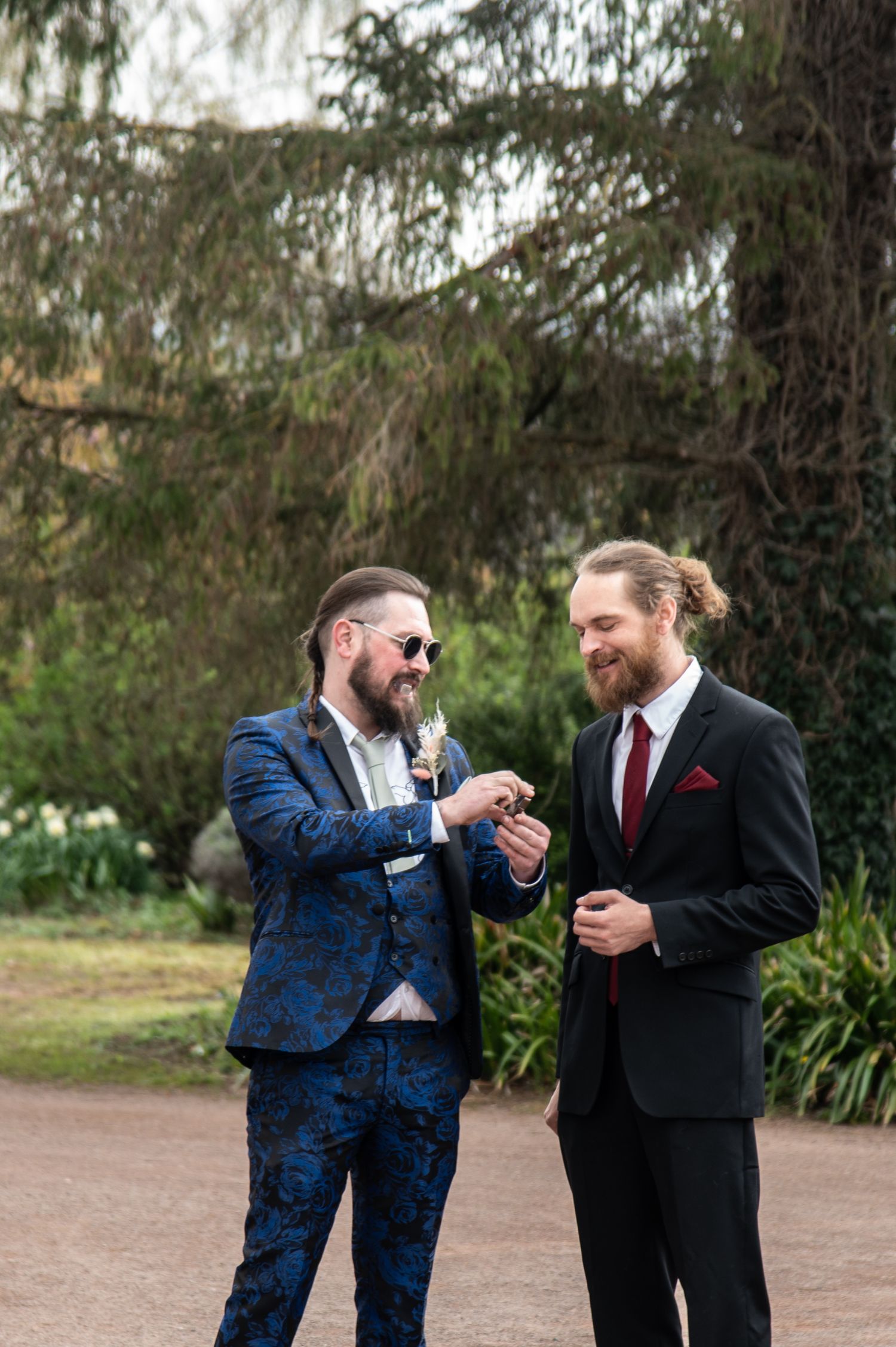 Two men in suits laugh and share a drink outdoors during a celebration.