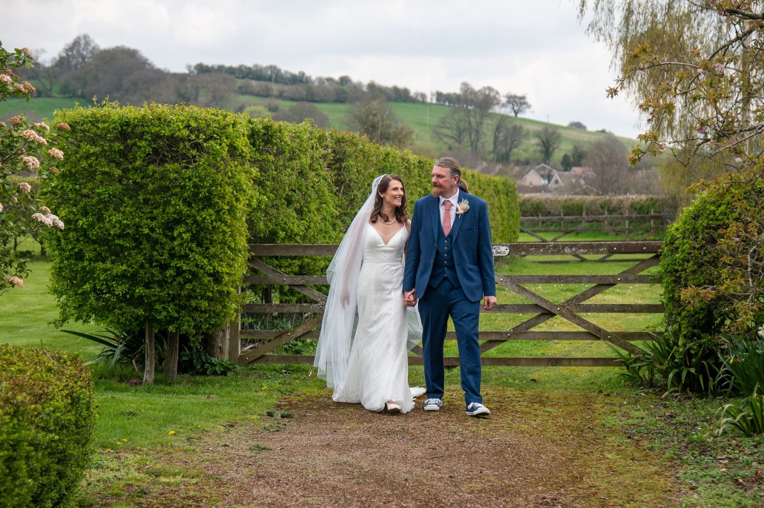 A couple shares a romantic moment by a rustic wooden gate in a garden setting.