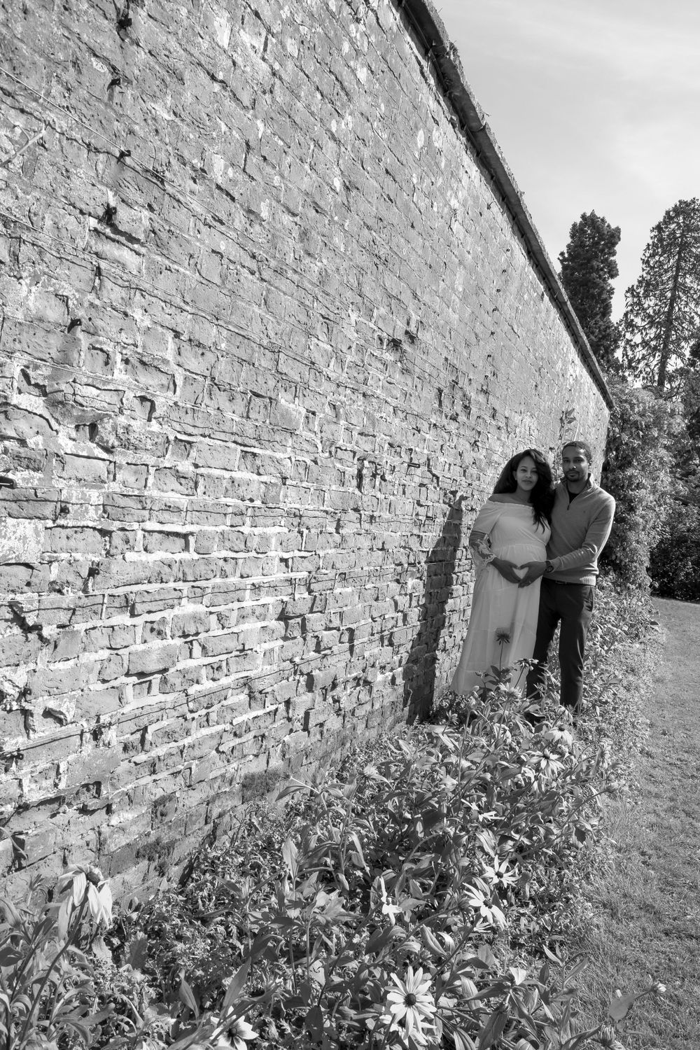 Black and white portrait of a couple standing against an old brick wall.