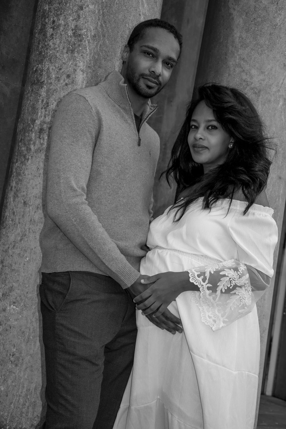 Intimate black and white portrait of an expectant couple posing against architectural columns.