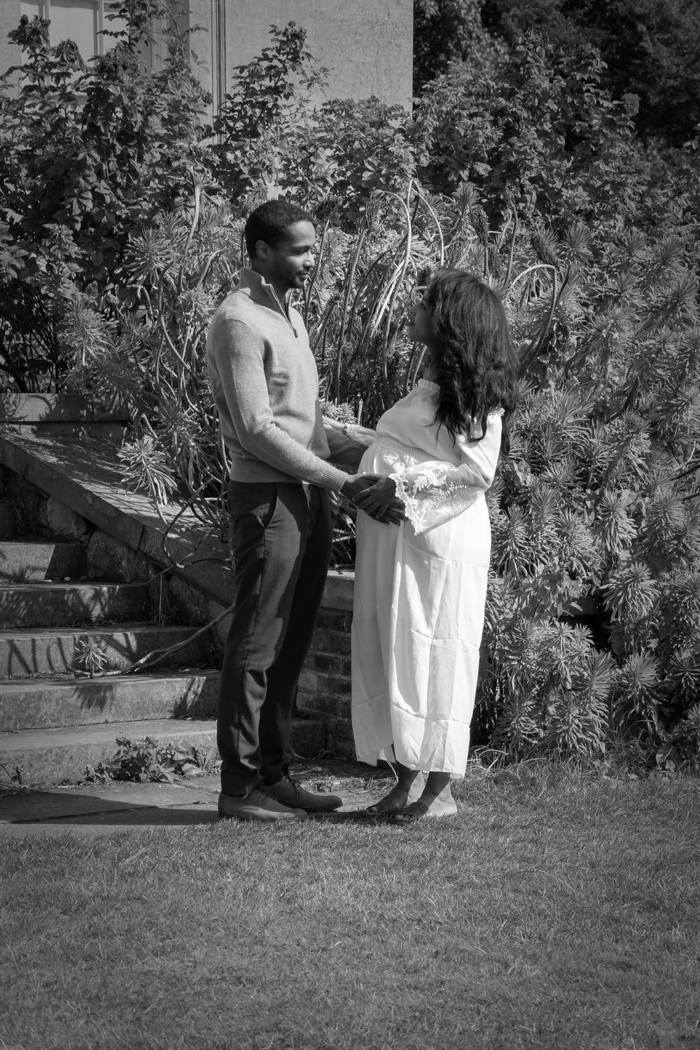 A romantic couple stands together in a garden setting in black and white photography.