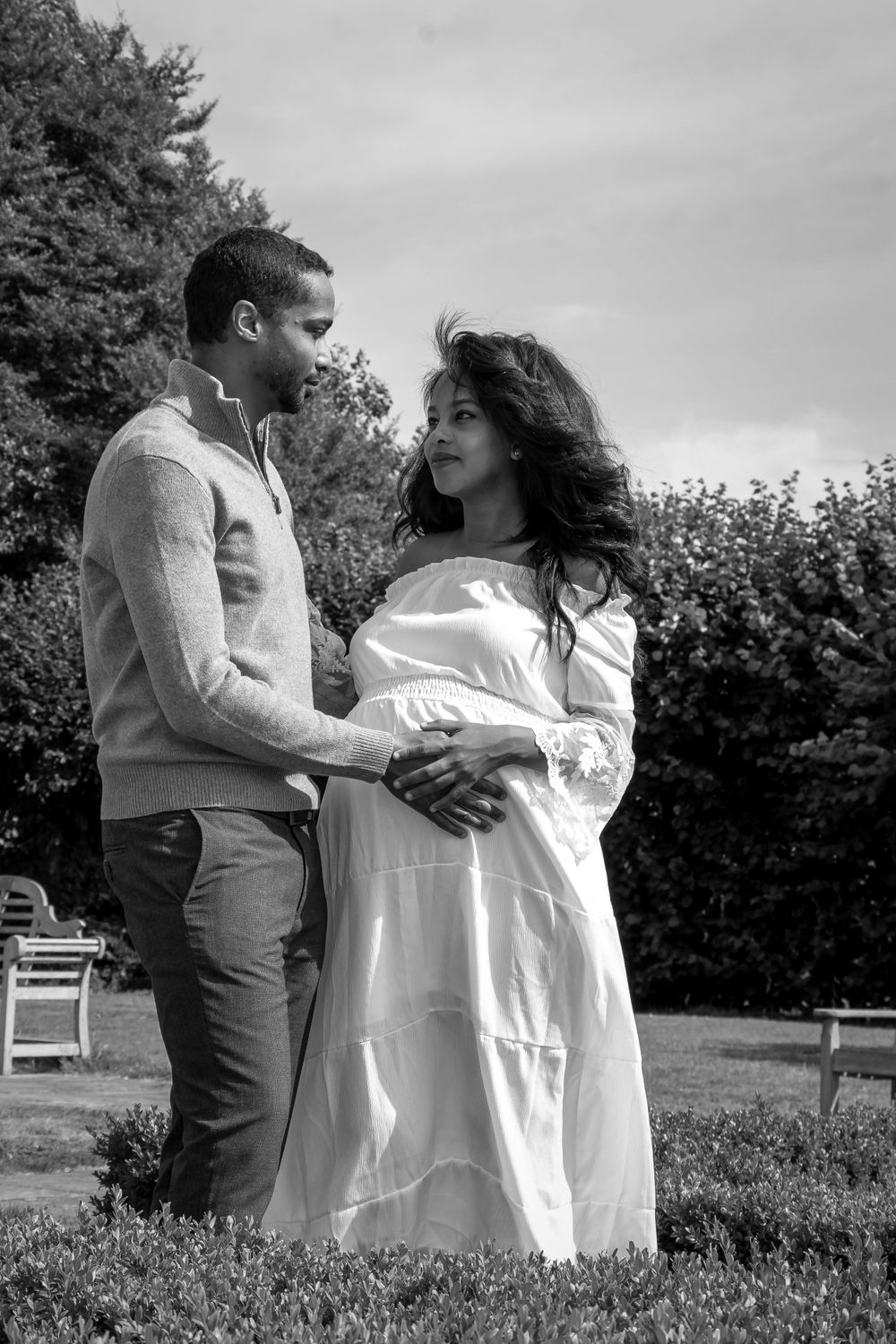 Romantic maternity photo of a couple in an outdoor garden setting captured in black and white.