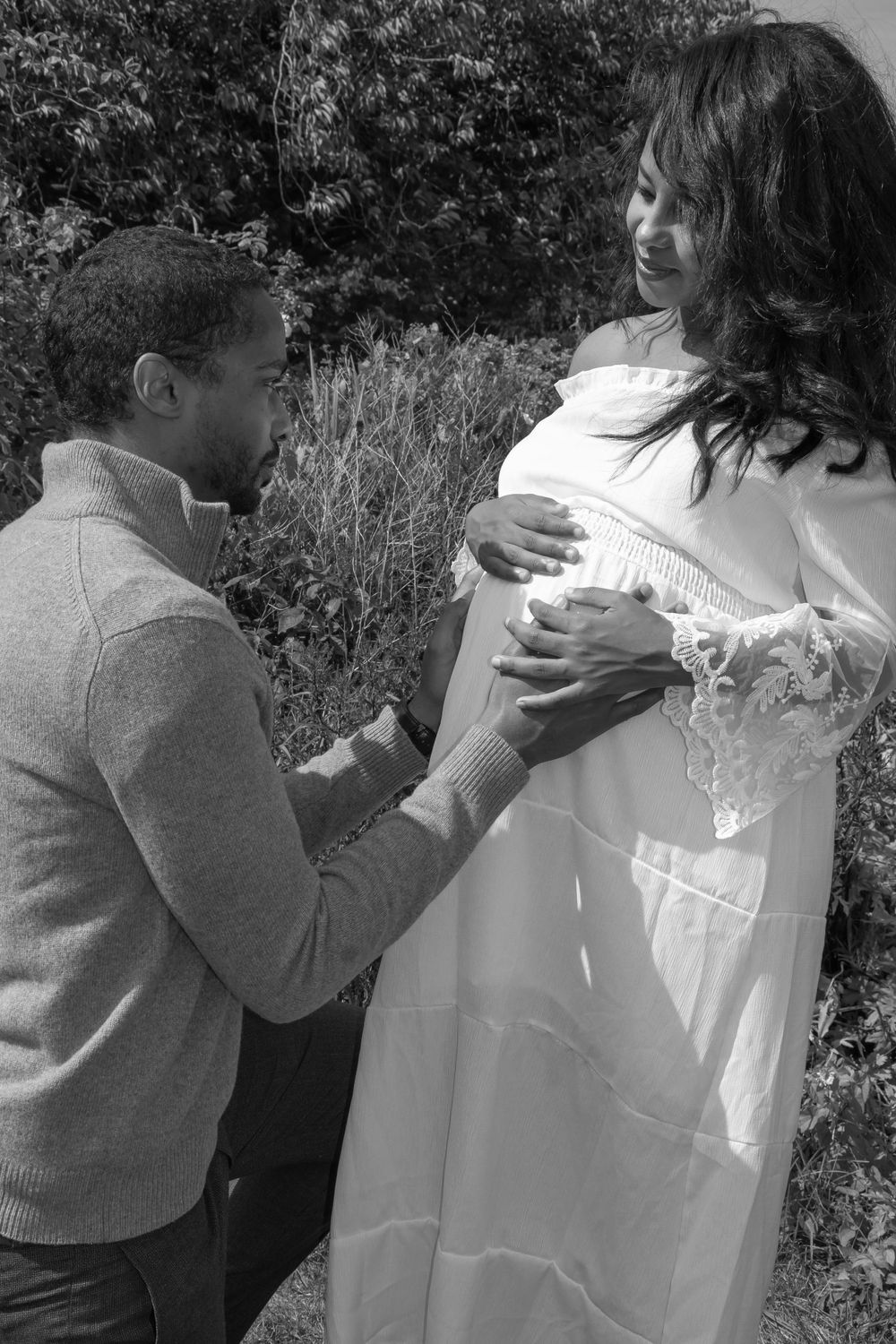 Tender maternity moment captured in black and white as couple poses in garden setting.