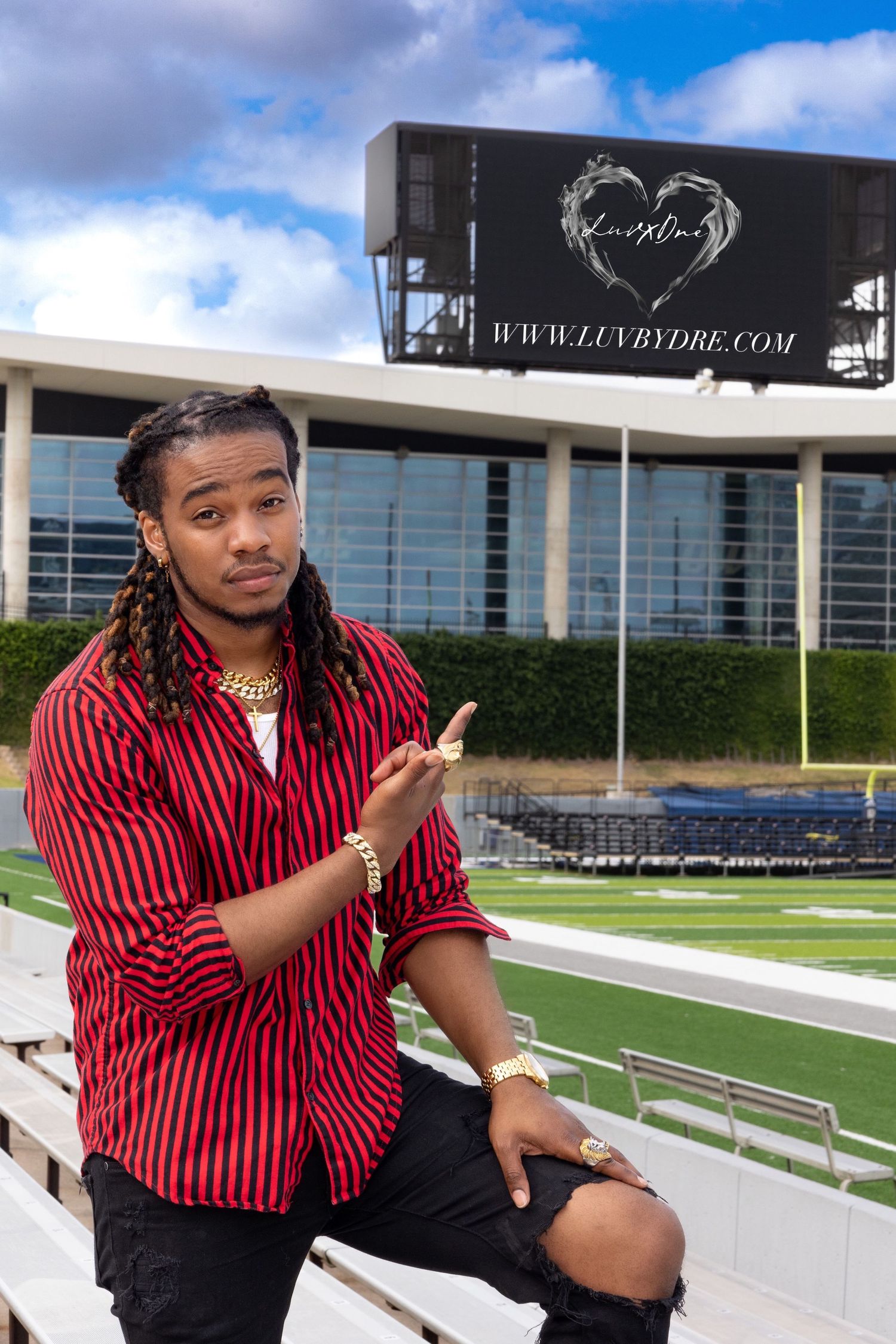 Person in red striped shirt and ripped jeans gestures while standing in stadium bleachers.