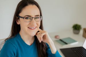 Professional working at desk with laptop in bright home office environment.