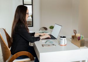 Side view of person working on laptop at white desk in home office setting.