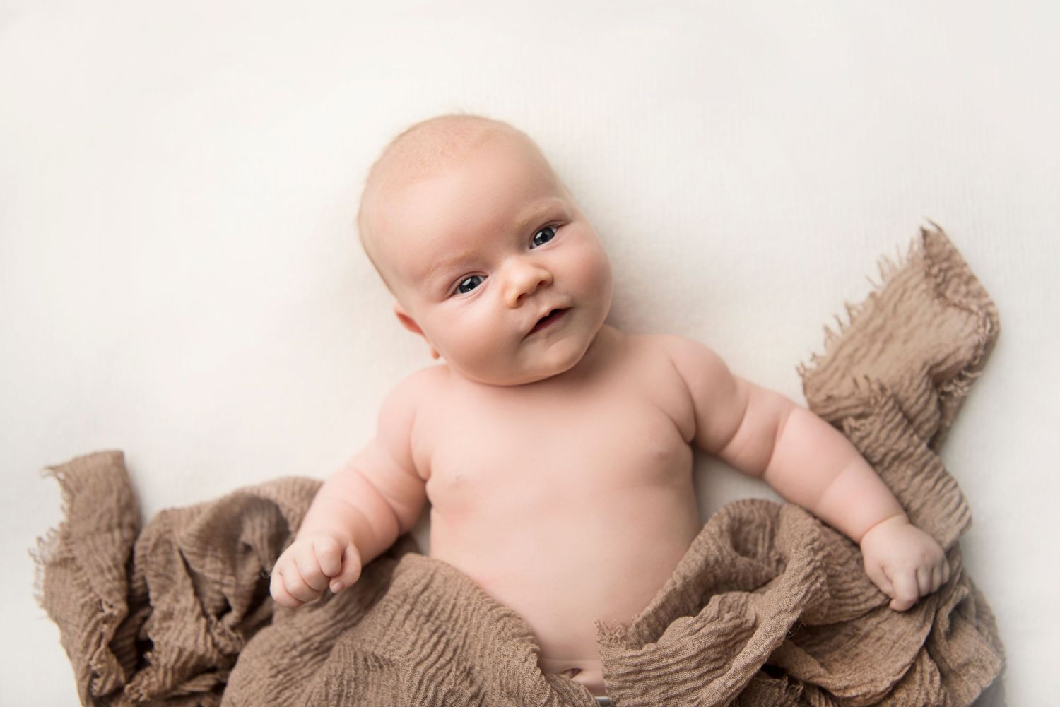 Baby lying on brown textured fabric during minimalist studio photography session.