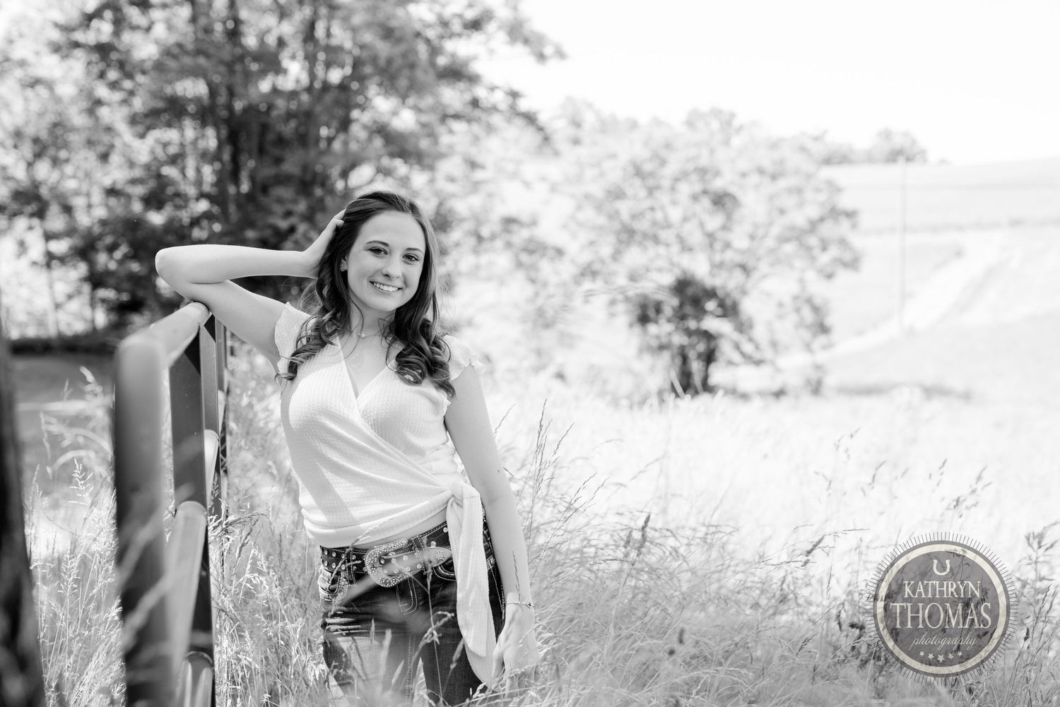 A black and white portrait leaning against a railing in tall grass.