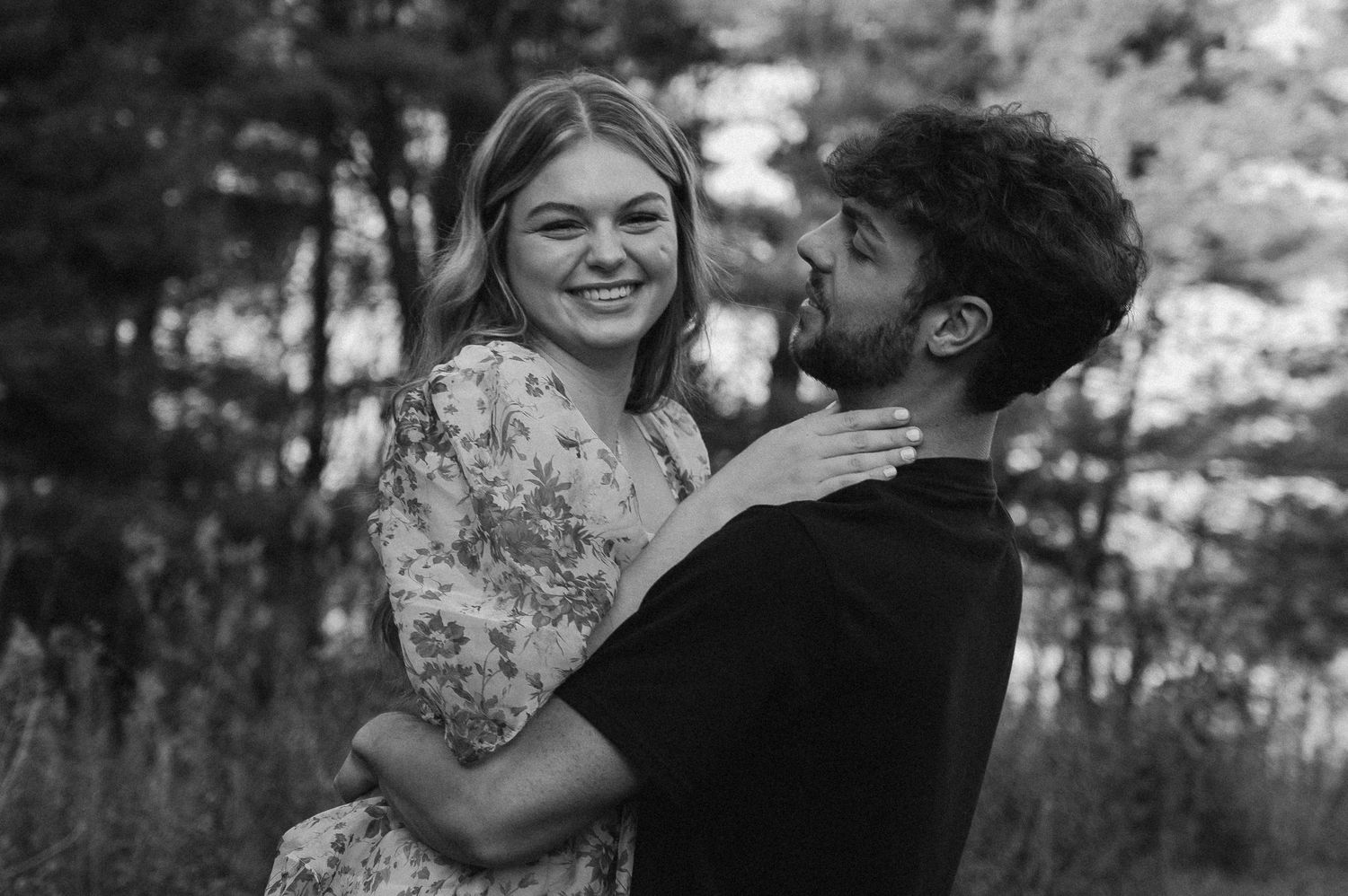 A tender moment captured between a couple laughing and embracing in a black and white outdoor portrait.