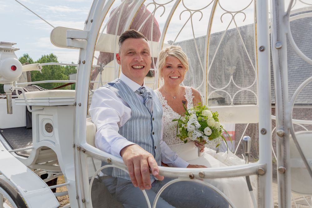 A couple sits in an ornate white carriage during their wedding celebration.