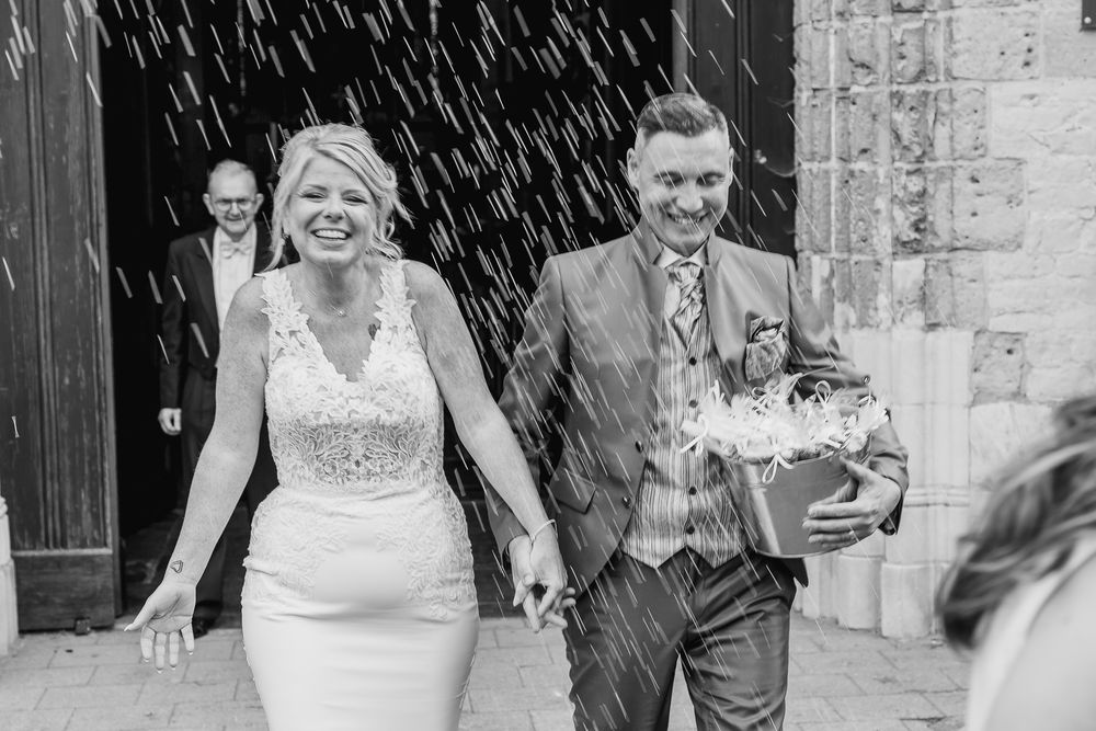 A joyful wedding exit under a shower of confetti in black and white.