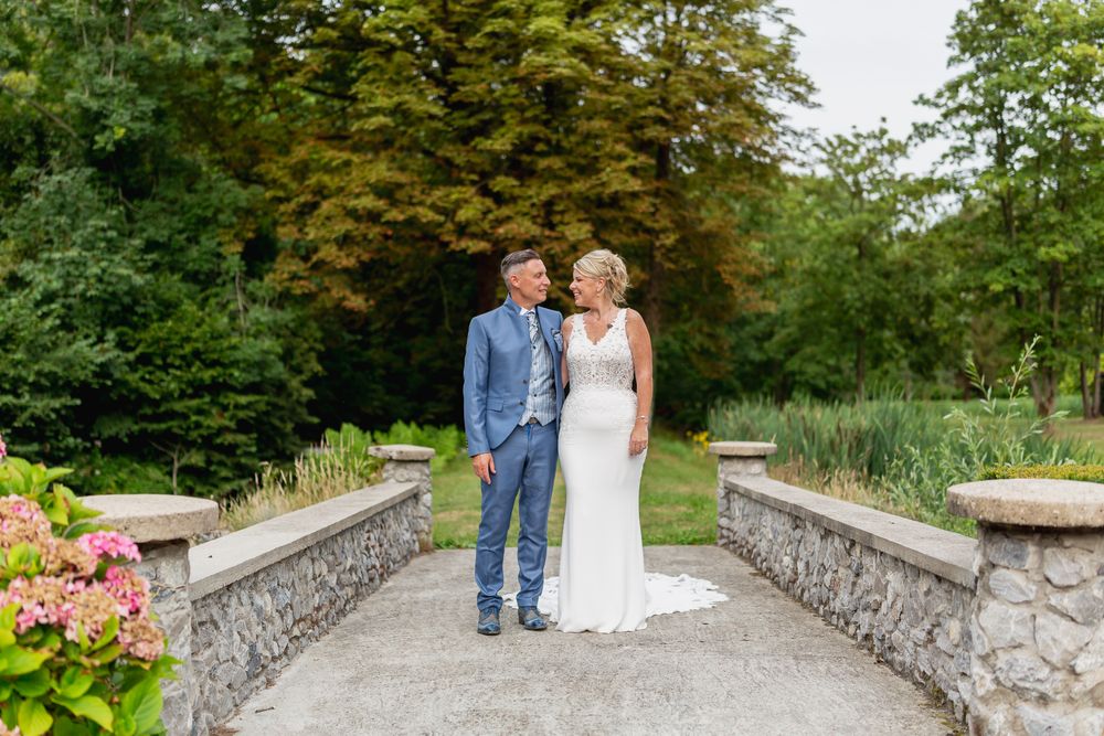 Couple stands on stone pathway in garden with pink hydrangeas and lush greenery.