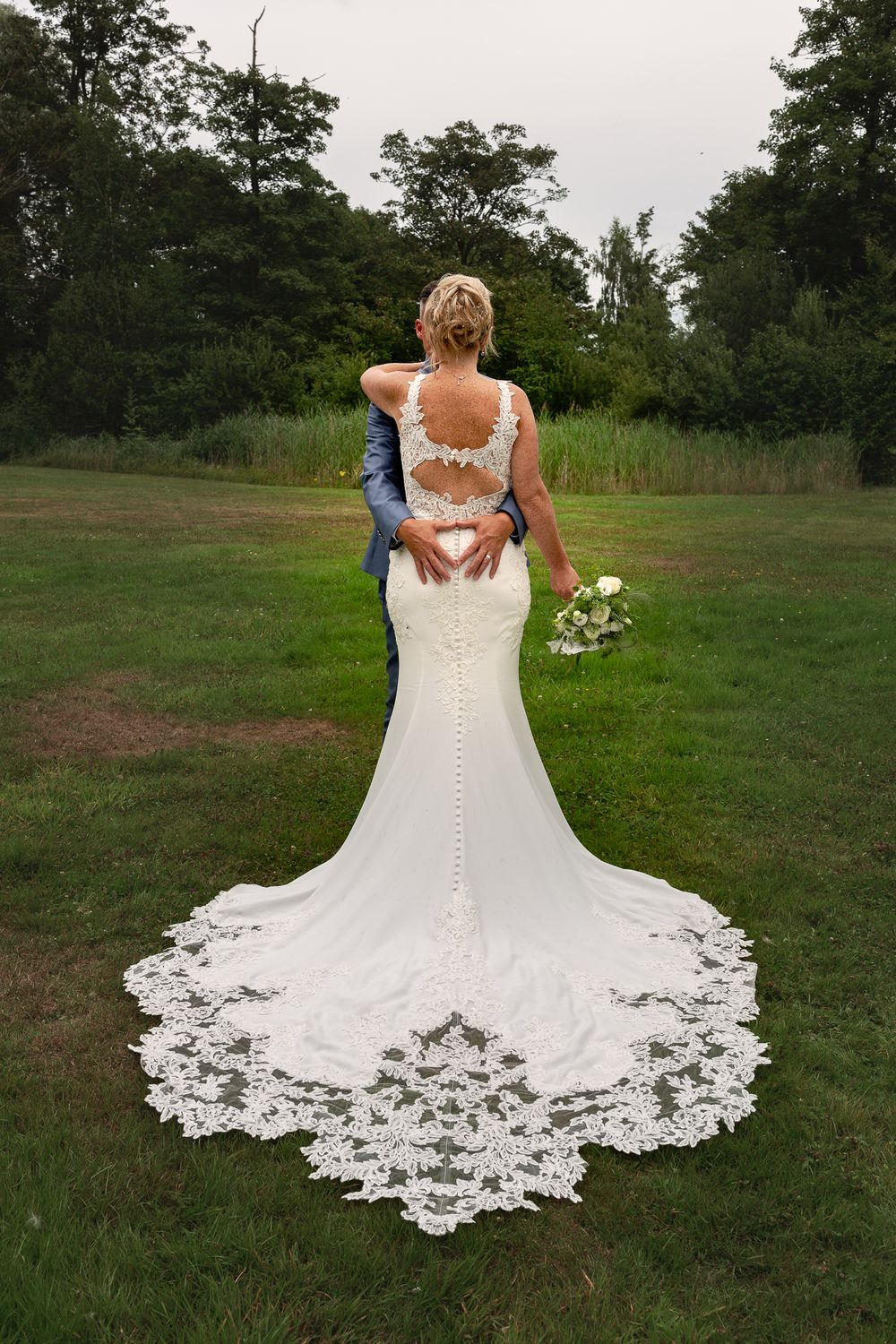 Back view of wedding dress with intricate lace train against green landscape.