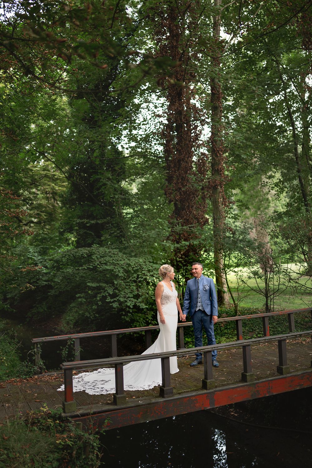 Couple standing on rustic wooden bridge surrounded by lush forest.