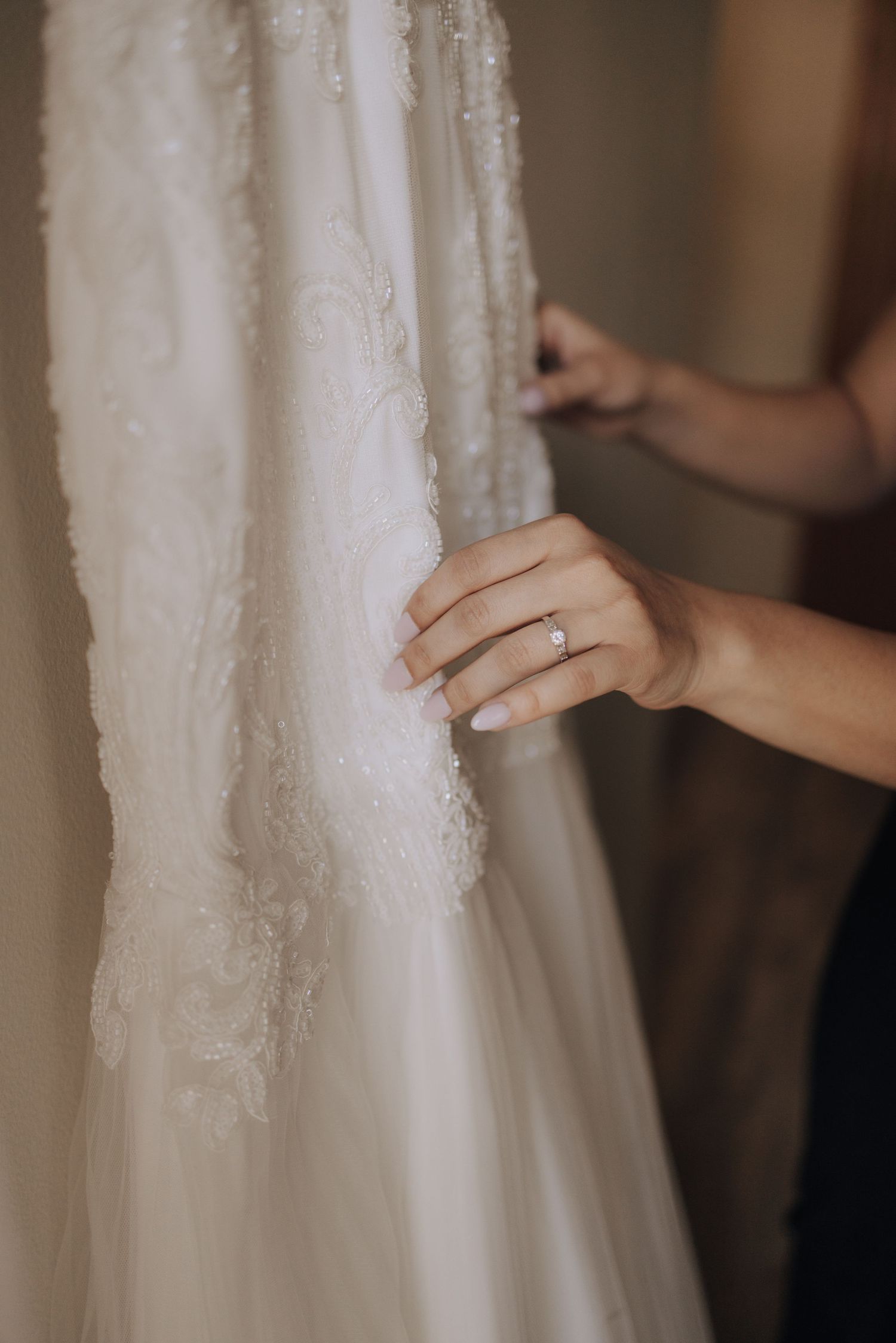 Hands gently touching the delicate lace details of a white wedding gown.