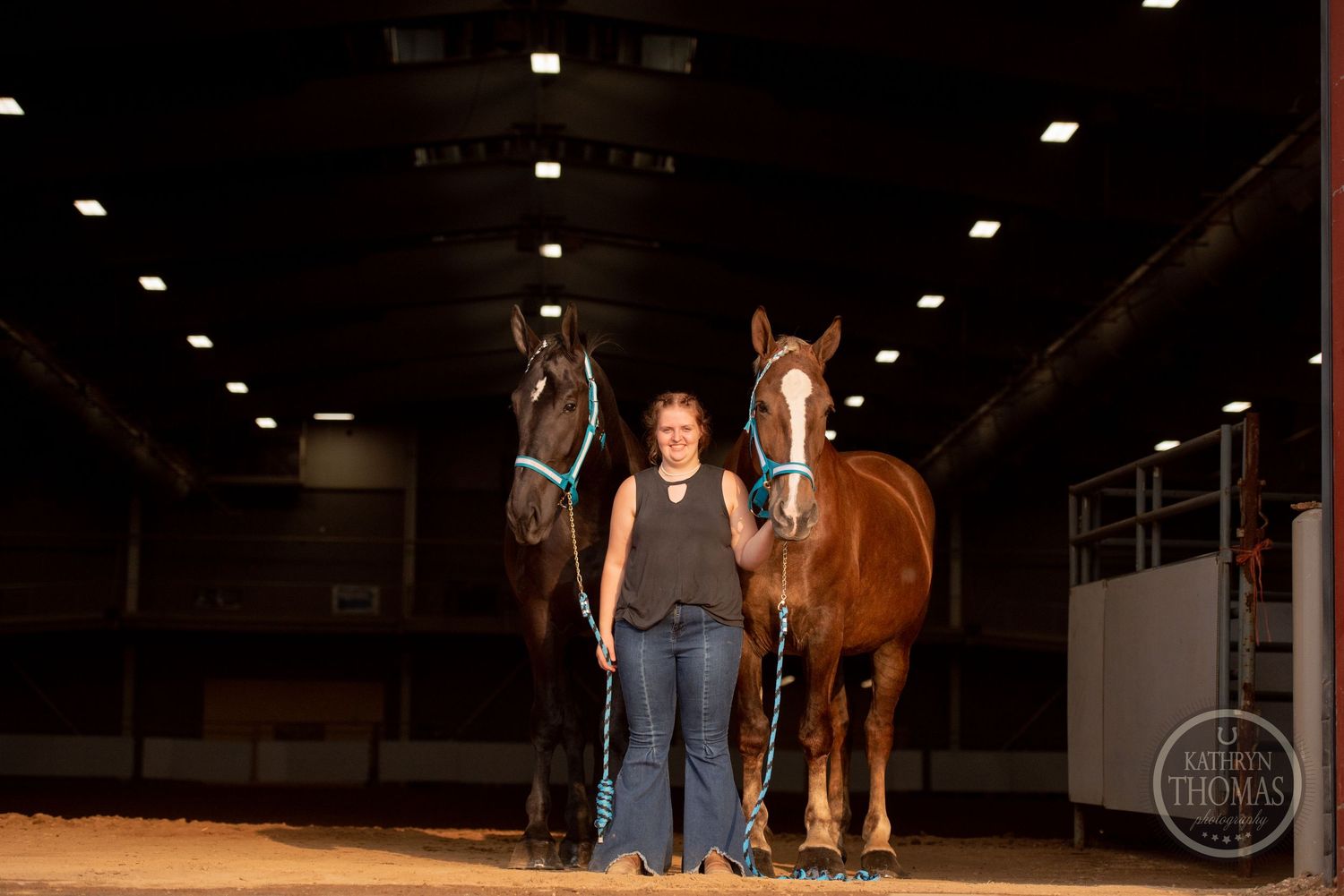 Two beautiful horses stand with their handler in an indoor riding arena under dim lighting.