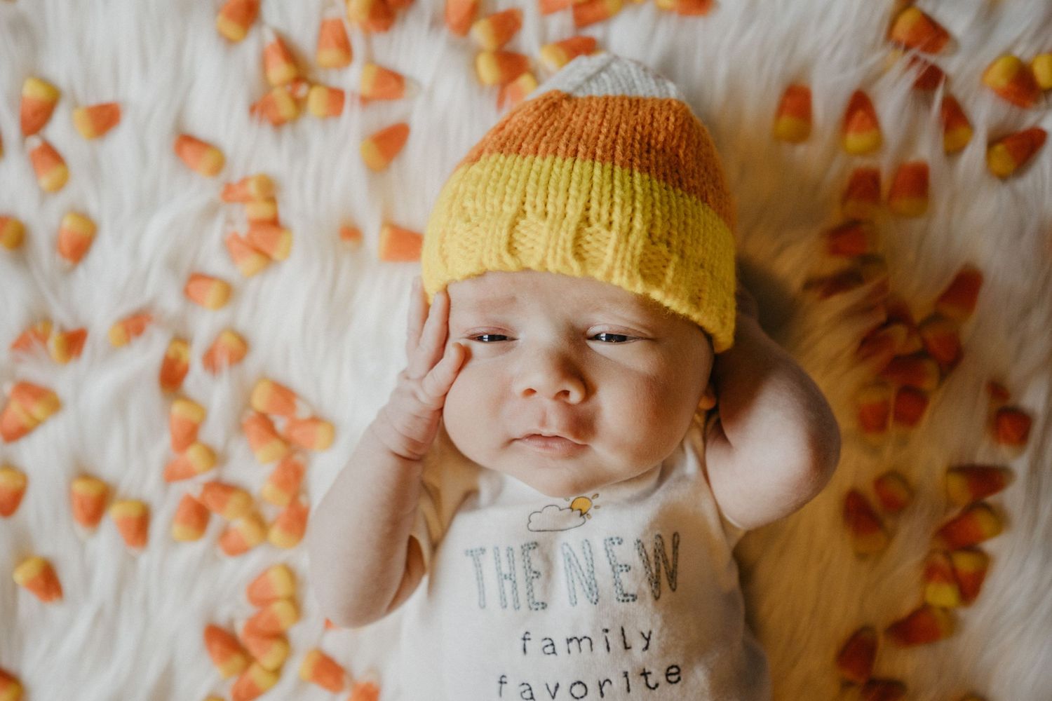 Baby wearing yellow knit hat lying on floral pattern blanket.