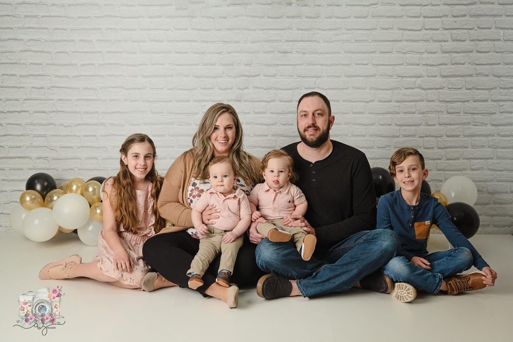 Family portrait against white brick wall with balloon garland decoration.