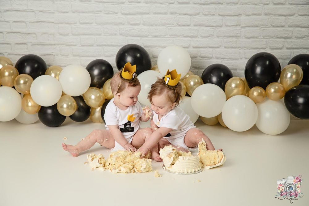 Smash cake photo with babies surrounded by destroyed cakes and balloon decorations.