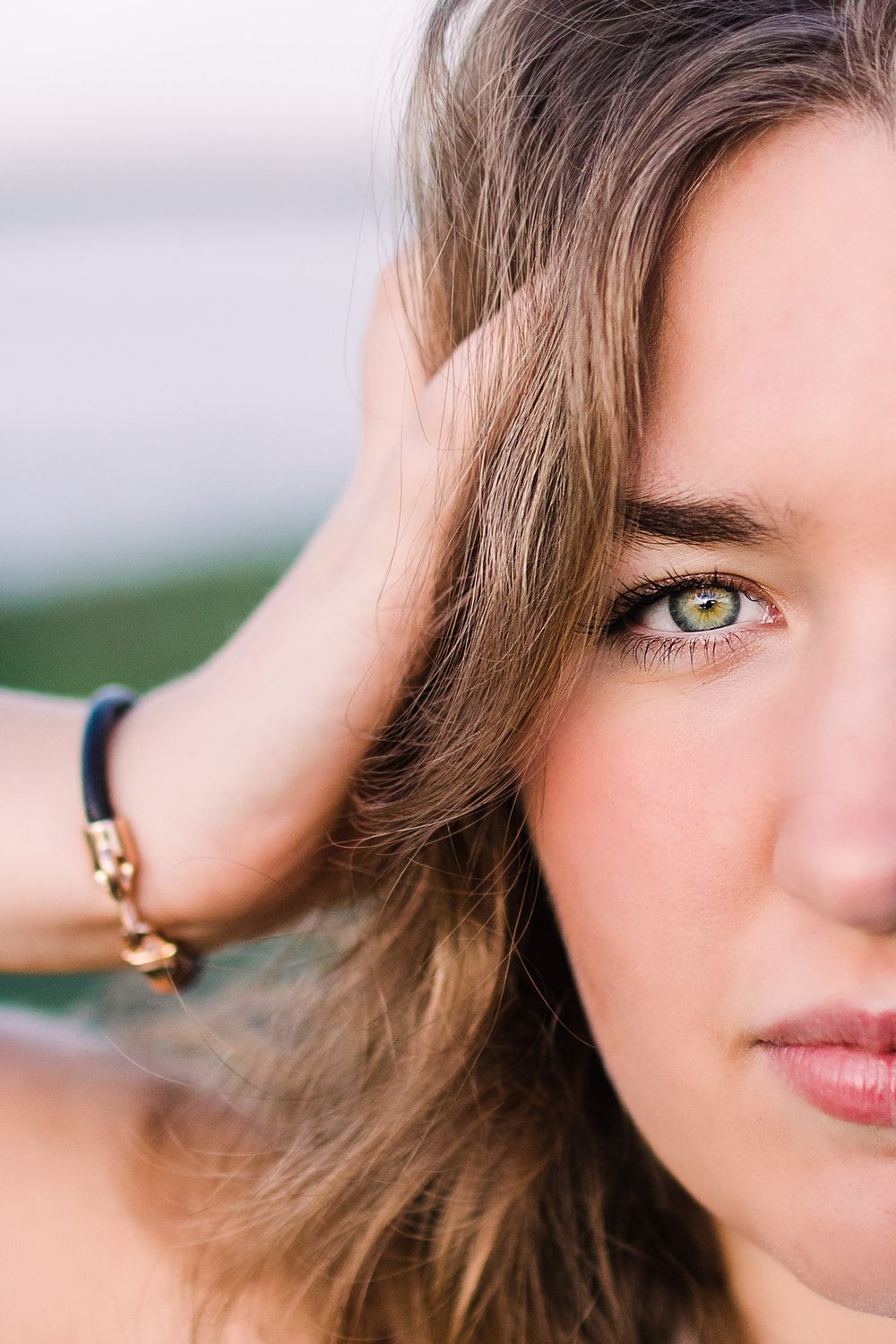 Close-up portrait of young woman with striking green eyes and bracelet pushing hair back.