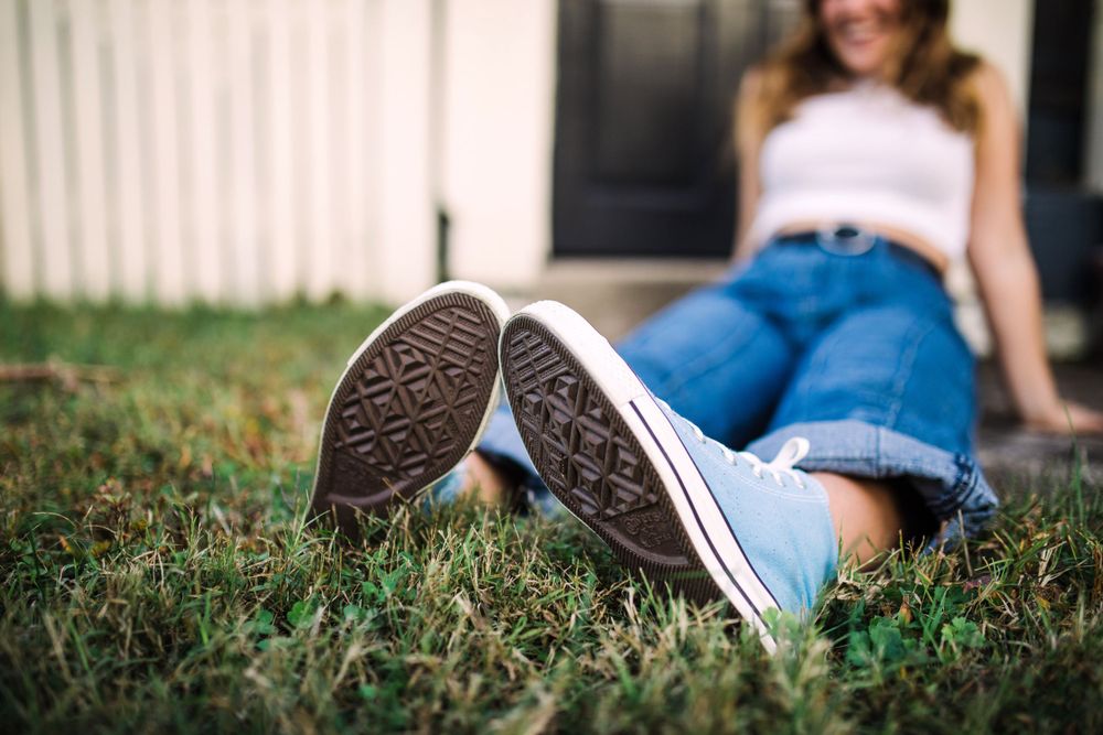 Young woman in Converse sneakers lying on green grass with a black door in the background.