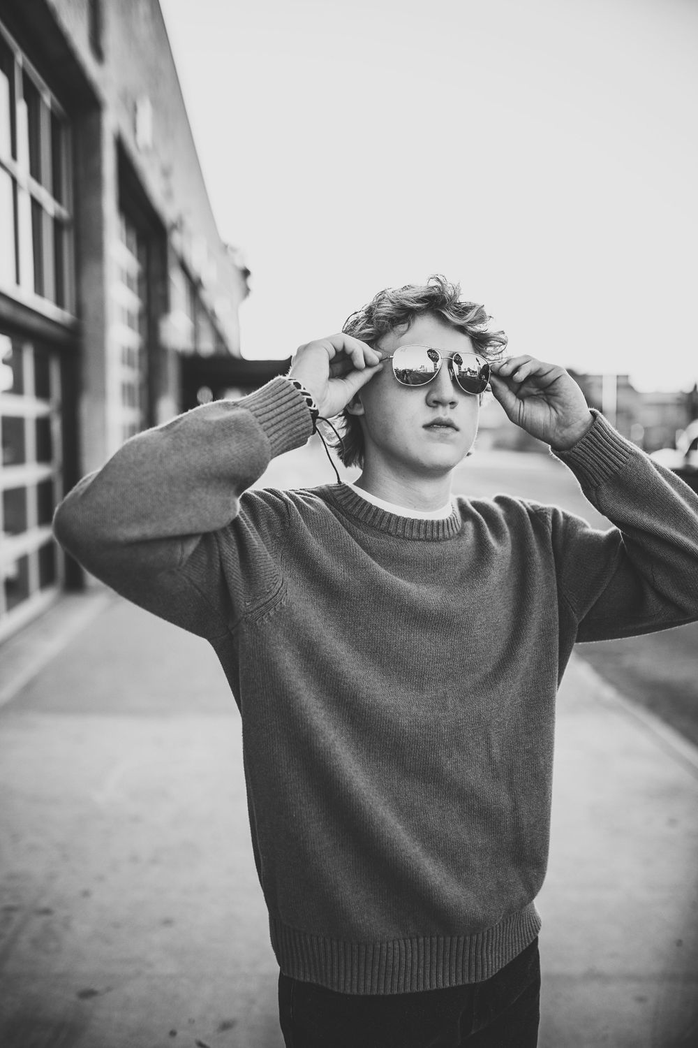 Teen boy adjusting sunglasses outdoors in a black and white urban portrait.