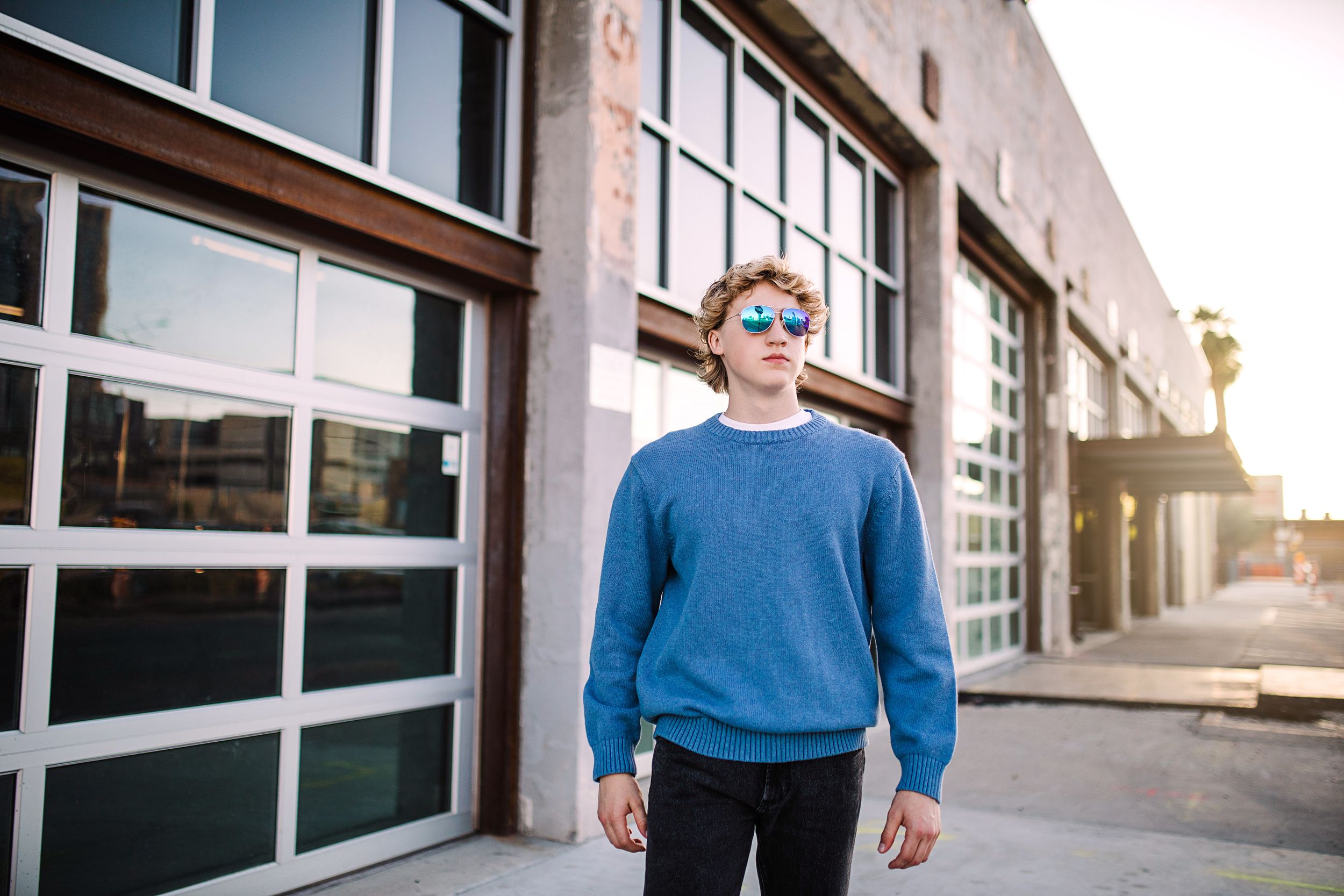 Young man in blue sweatshirt standing before modern building with large windows.