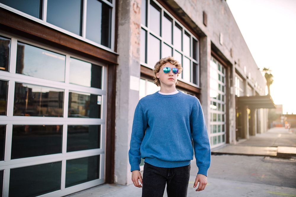 Young man in blue sweatshirt standing before modern building with large windows.