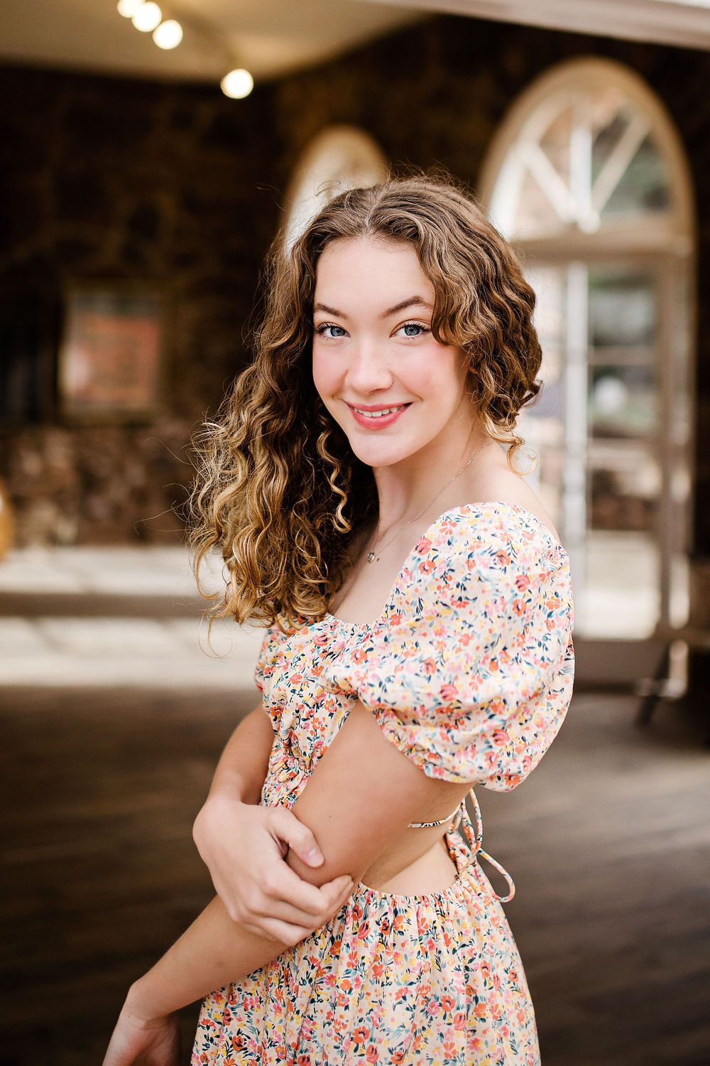Smiling young woman with curly hair in floral crop top and skirt set outdoors.
