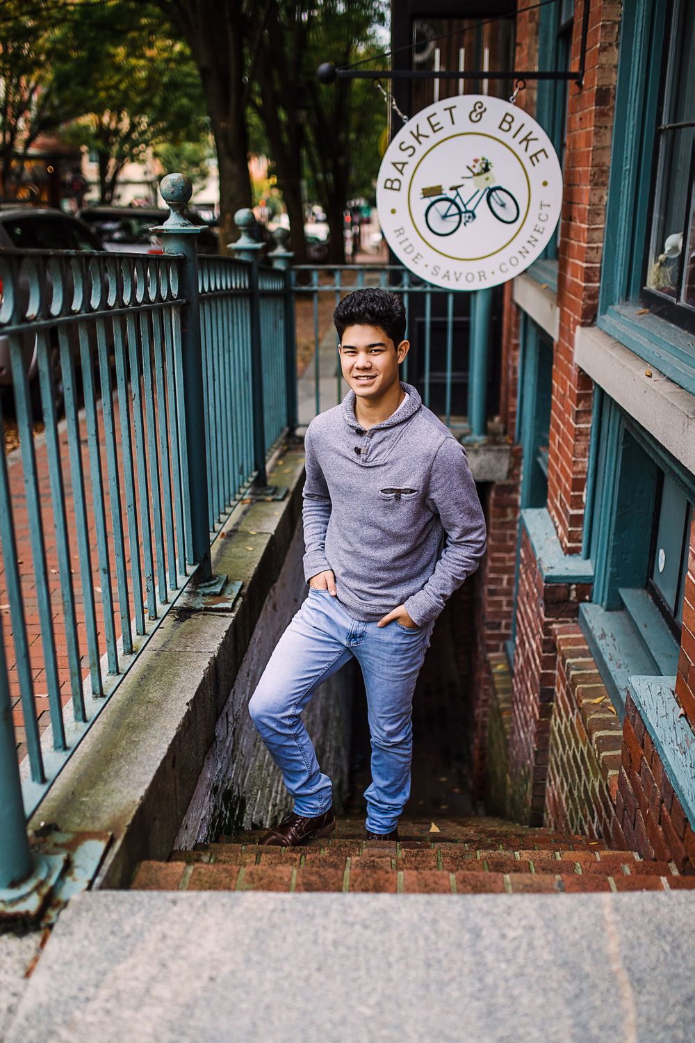 Young man posing on steps beside Basket and Bike shop sign with teal railing.