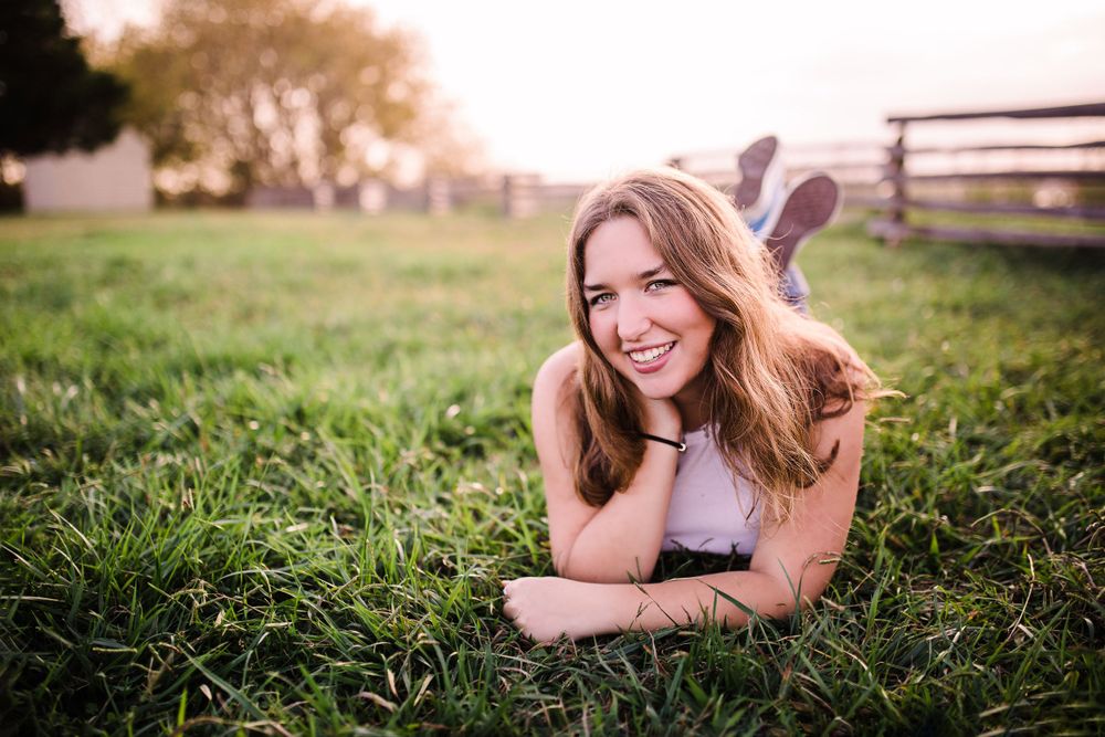 Smiling young woman with long hair lies on green grass in golden sunset light.
