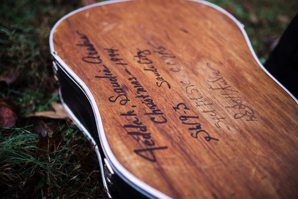 Close-up of a wooden acoustic guitar case with handwritten signatures and messages on its surface.