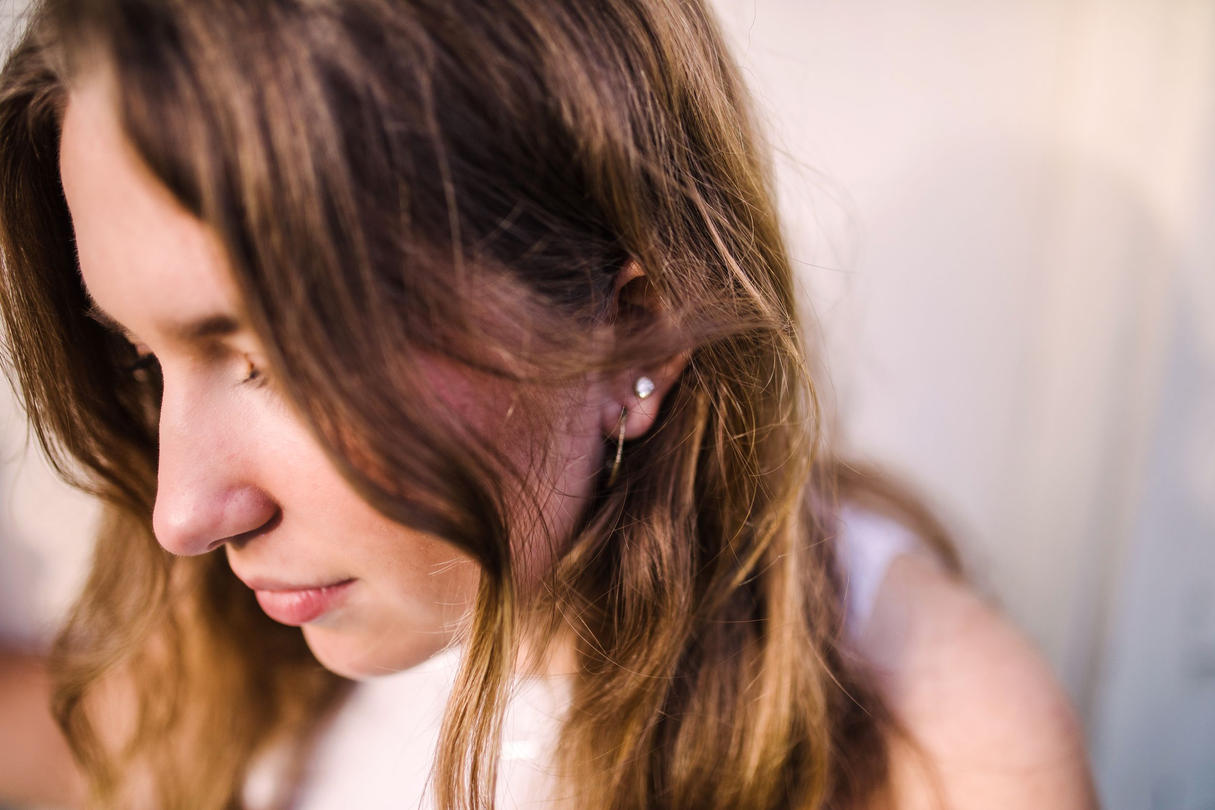Close-up portrait of a young woman with brown hair and small stud earring looking down.