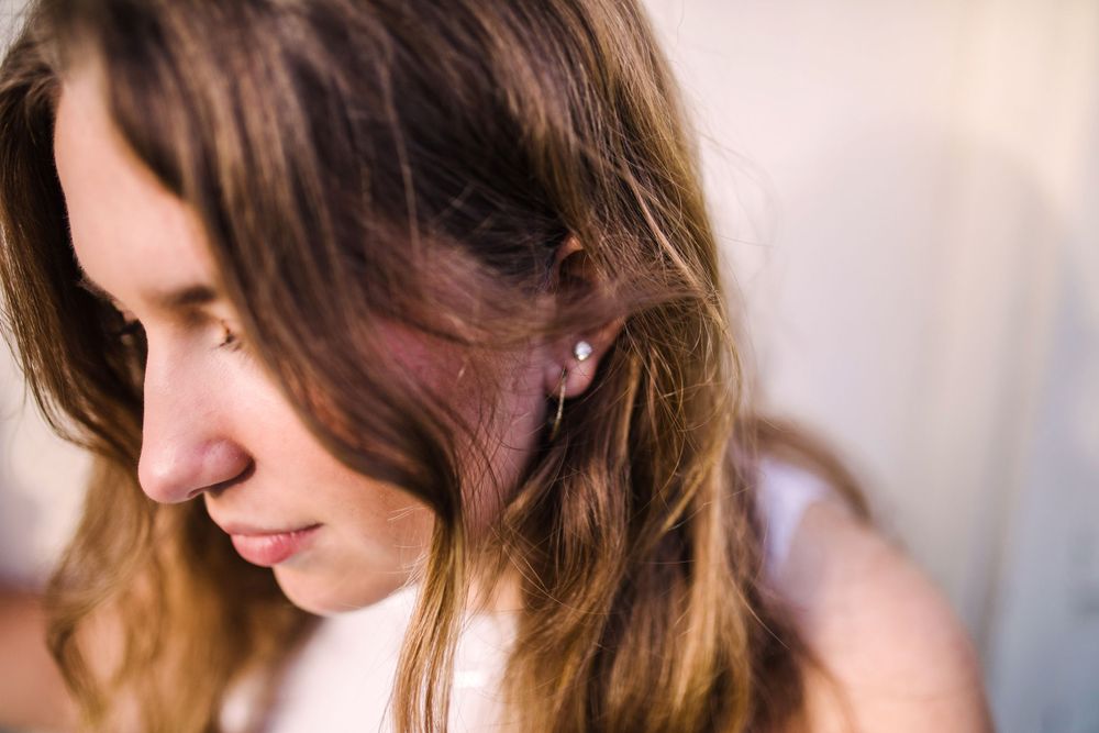 Close-up portrait of a young woman with brown hair and small stud earring looking down.