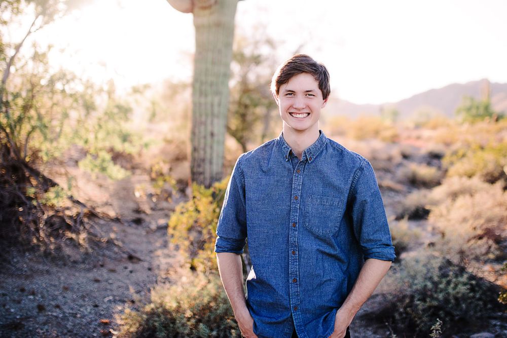 Happy young man in blue denim shirt smiling in sunny desert landscape with cactus.