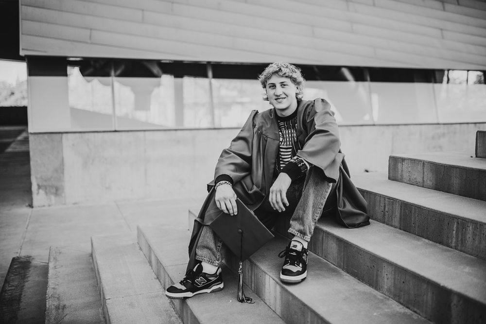 Black and white photo of teen boy sitting on concrete steps with skateboard.