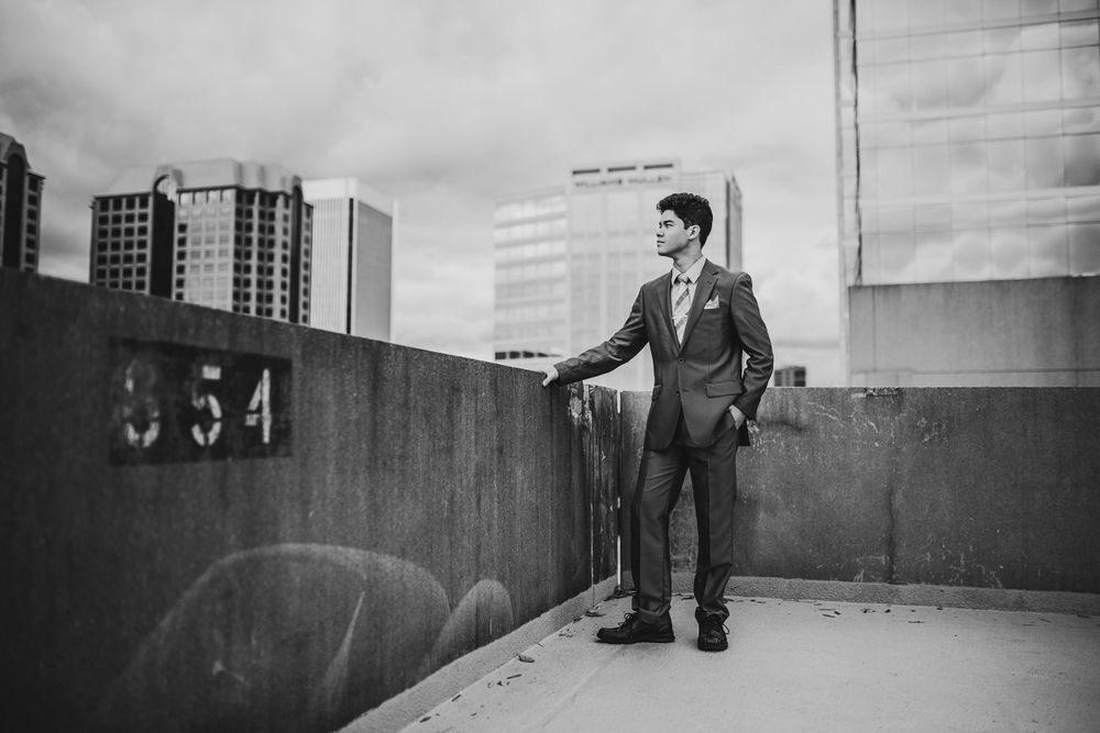 Stylish young man in suit standing on rooftop with city skyline in black and white.