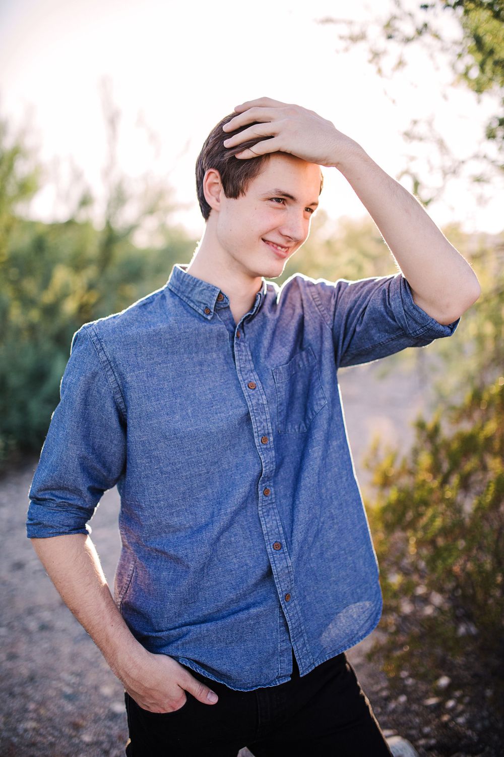 Young man in blue shirt running hand through hair in golden sunset light.