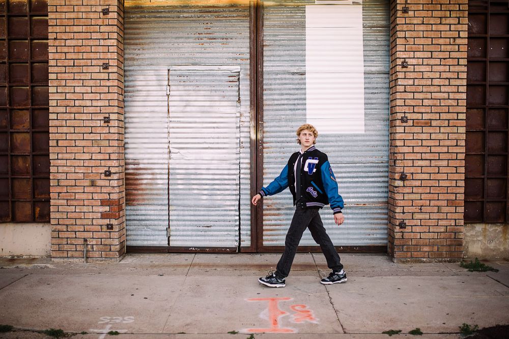 Young man walking confidently past a brick building with a metal garage door.