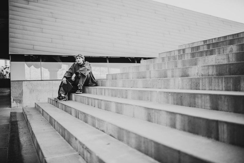 Black and white photo of young man sitting alone on wide concrete outdoor staircase.