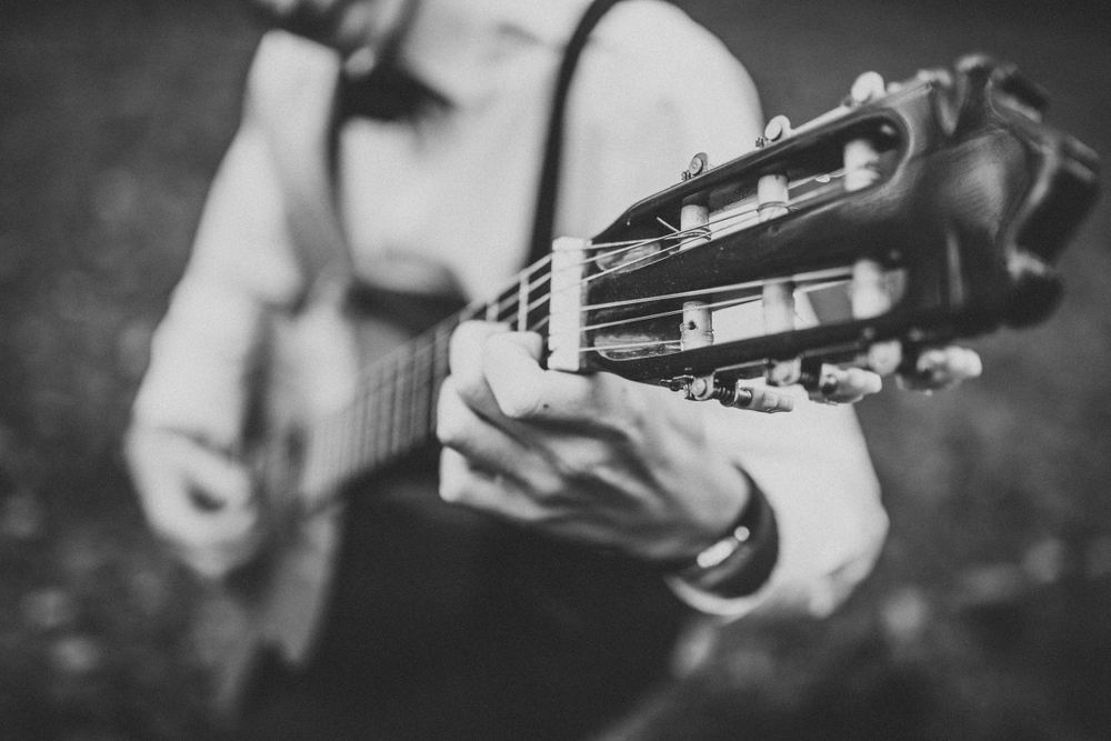 Black and white photo of hands playing classical acoustic guitar outdoors in natural setting.