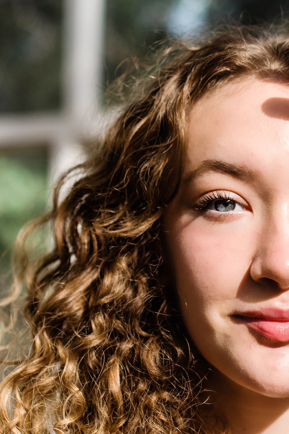Close-up half portrait of young woman with curly hair and blue eyes in natural sunlight.